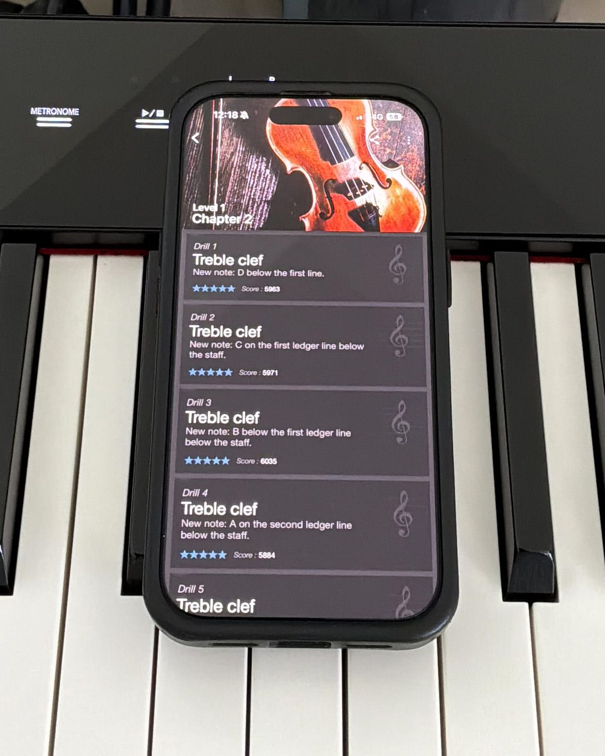 Complete Music Reading Trainer on an iPhone lying on a digital piano, showing the drill list for Level 1 Chapter 2 — five treble-clef drills, each introducing one new note and each scored five stars.